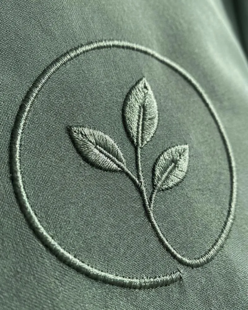 Close-up of a tone-on-tone satin-stitch embroidered logo on sage scrub fabric.